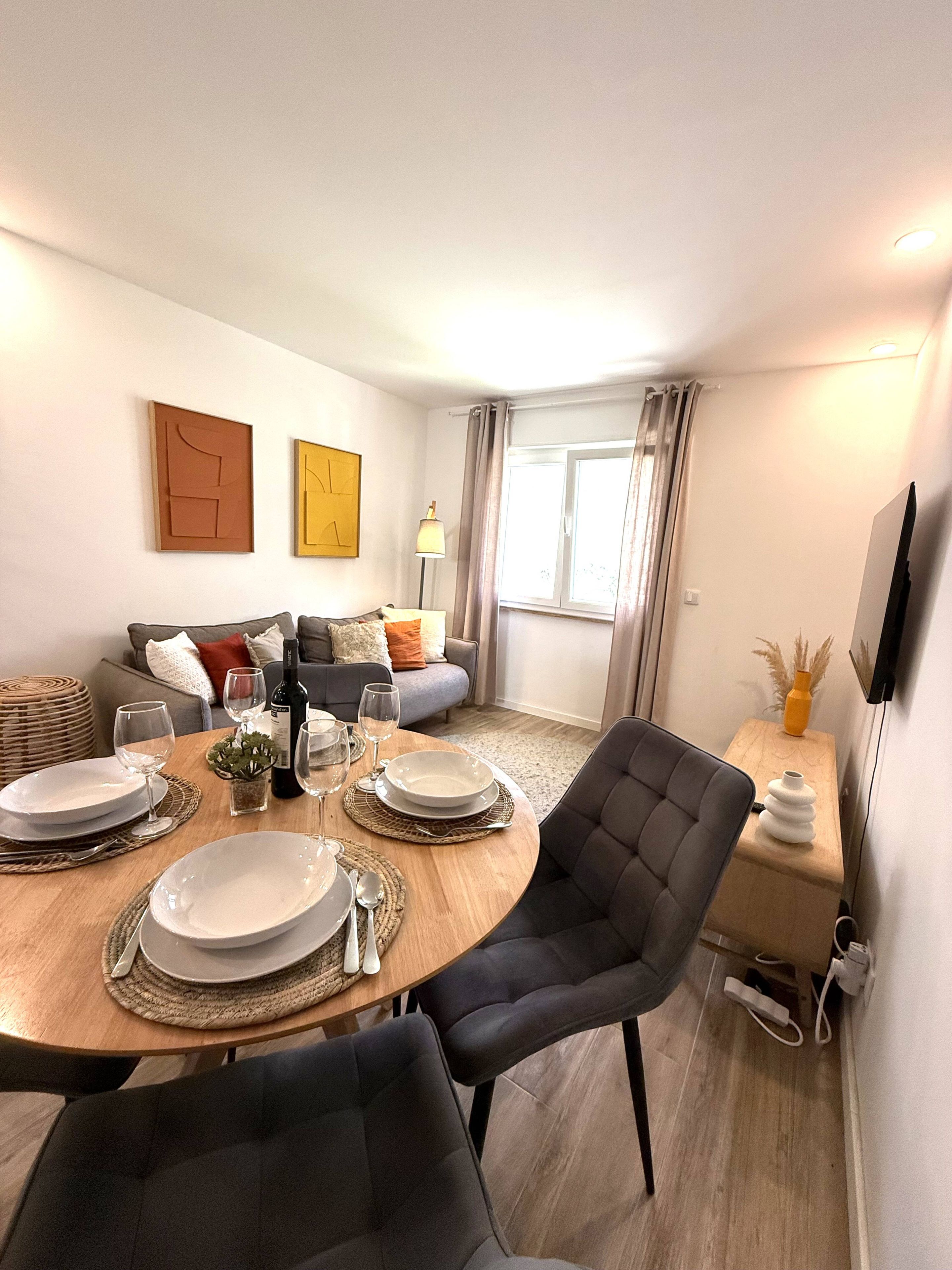 Een moderne woonkamer met een eethoek, een zithoek en een flatscreen televisie aan de muur.