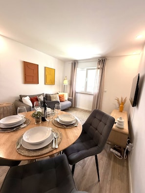 A modern living room with a dining area, a sofa set, and a flat-screen TV mounted on the wall. - Charming Apartment near Parede Beach (Cascais)