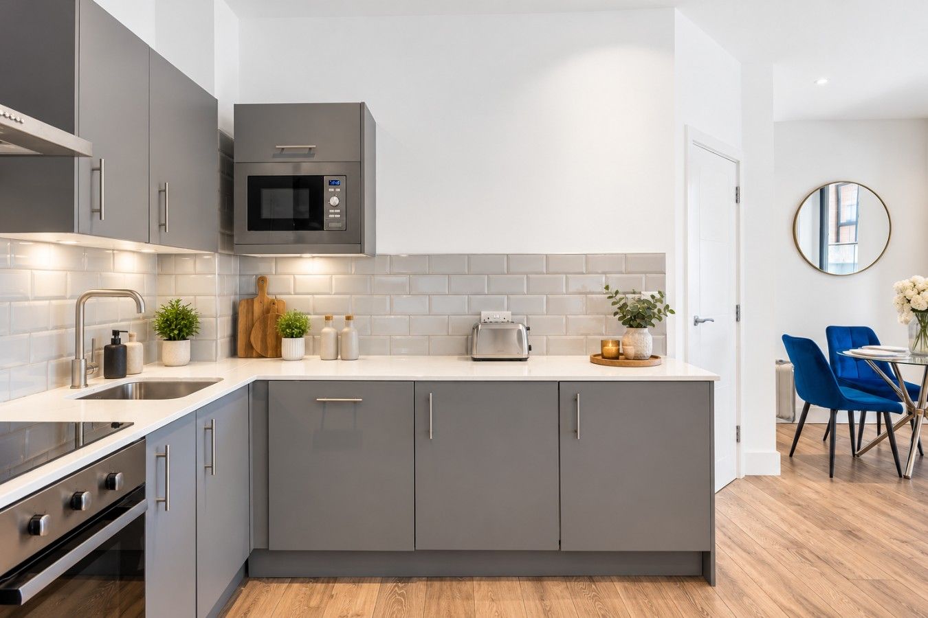 A modern kitchen with grey cabinetry, a microwave, a toaster, and a dining area with blue chairs.