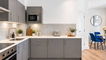A modern kitchen with grey cabinetry, a microwave, a toaster, and a dining area with blue chairs.