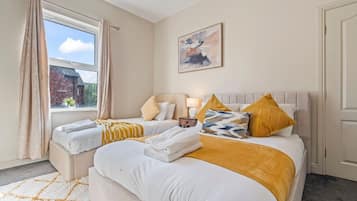 A hotel room with two beds, a window with curtains, a painting on the wall, and a door.