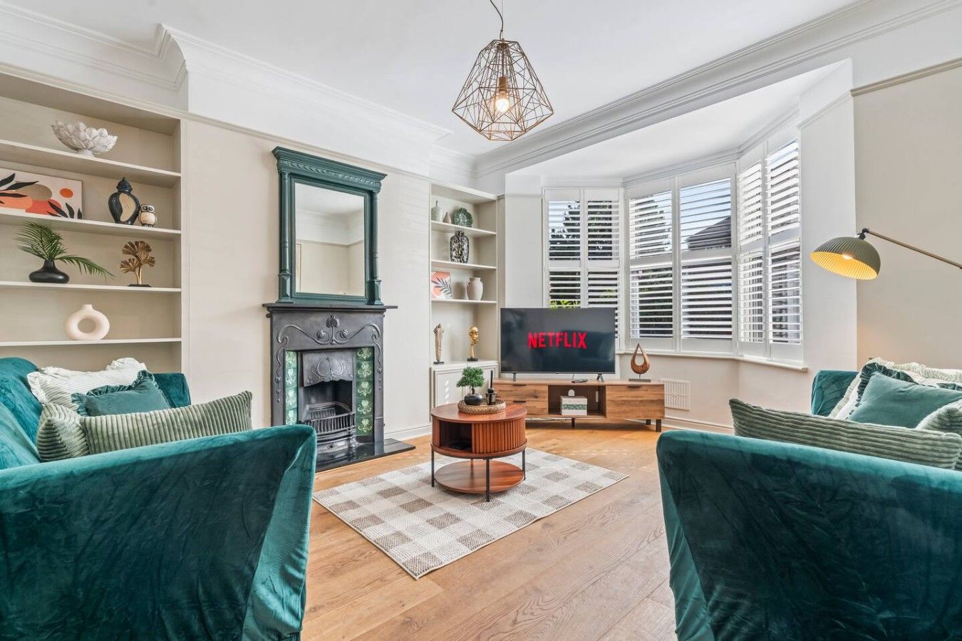 A living room with teal sofas, a fireplace, a television, and a large window with blinds.