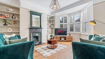 A living room with teal sofas, a fireplace, a television, and a large window with blinds.