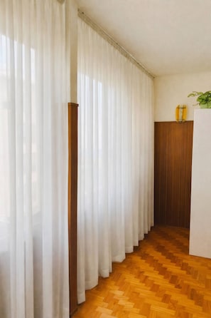 Una habitación con piso de parqué de madera, cortinas blancas y un armario de madera.