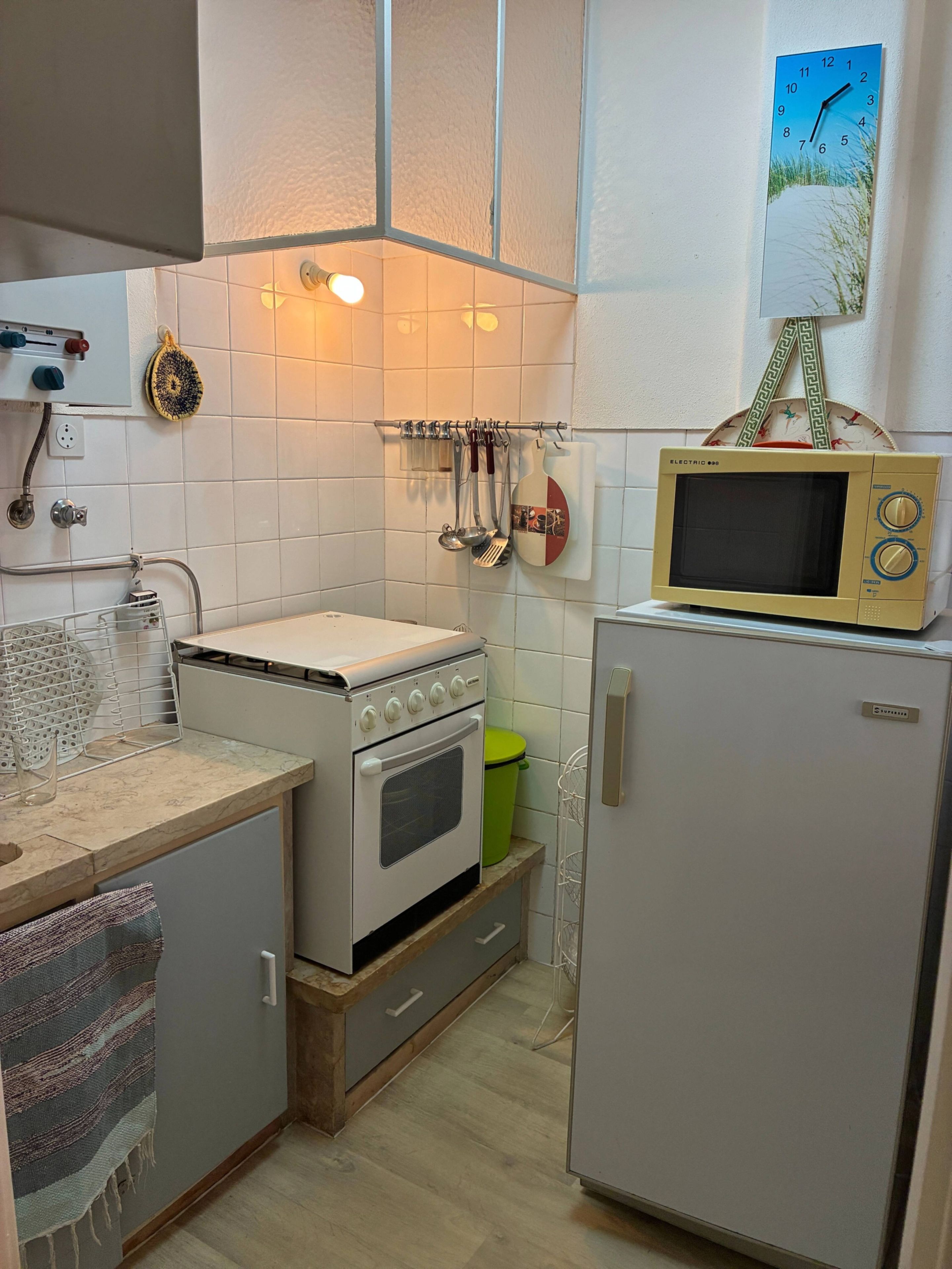 Una cucina con elettrodomestici bianchi, un forno a microonde sopra il frigorifero e un espositore a parete per utensili.