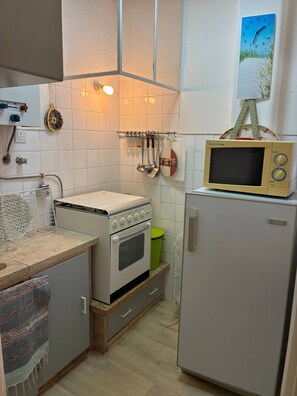 Una cocina con electrodomésticos blancos, un microondas sobre un refrigerador y un colgador con utensilios.