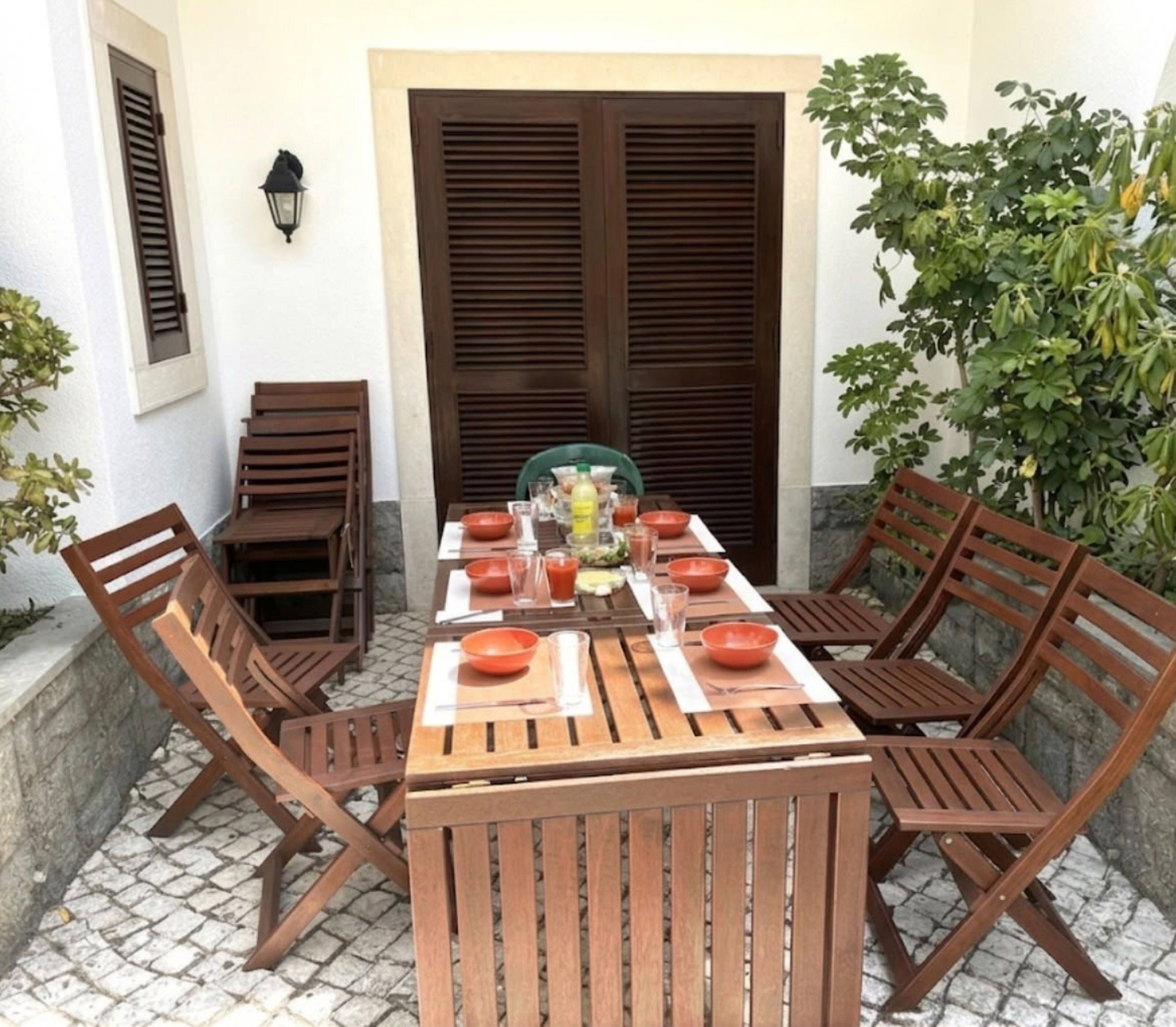 A wooden table set for dining with chairs, a potted plant, and a door with shutters.
