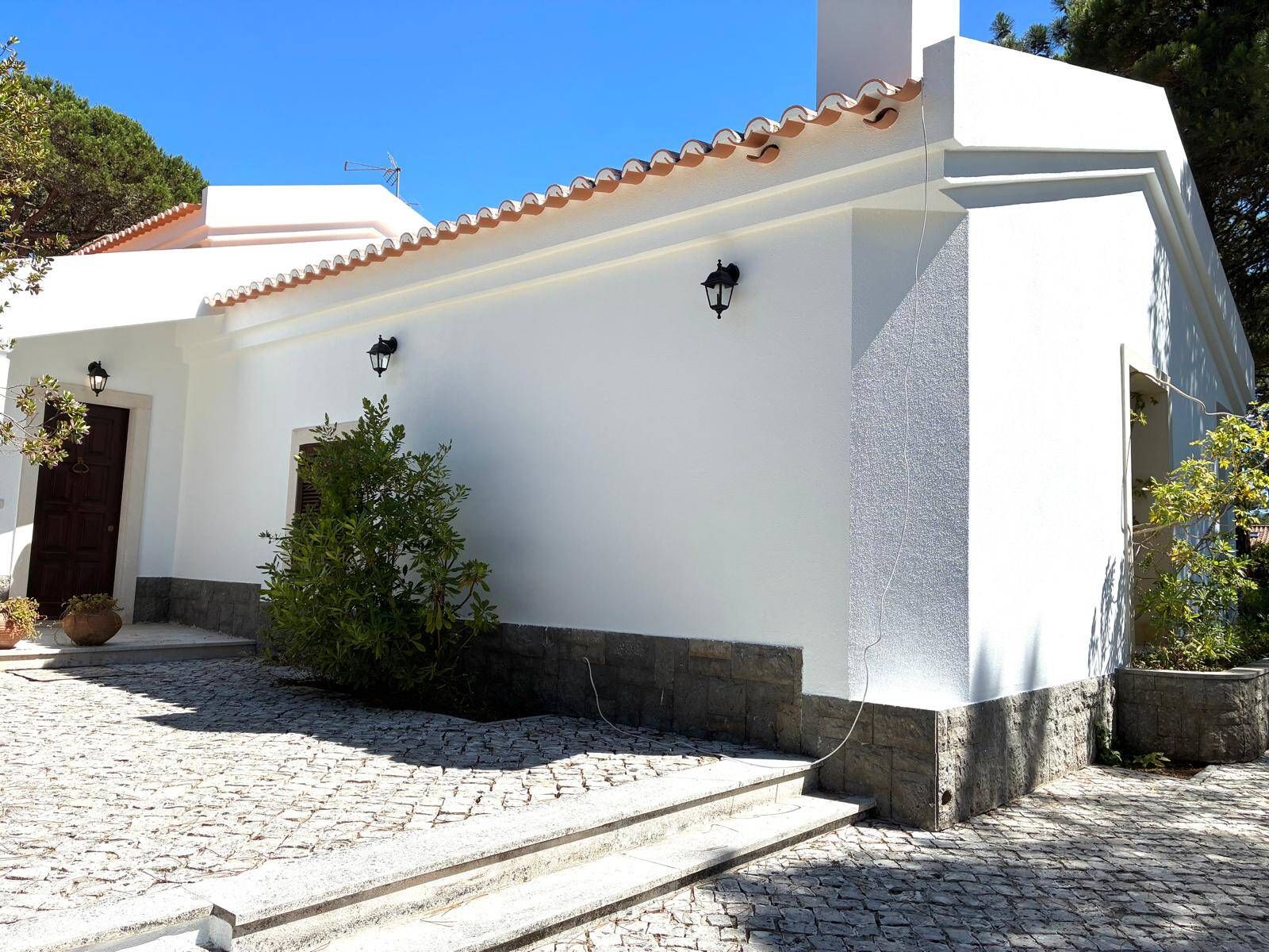 A building with a white facade, a tiled roof, and a cobblestone entrance.