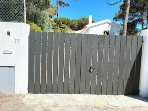 A gated entrance with a number '77' on a white wall, a metal fence, and a clear sky. - Pinewood Beach Villa- Colares (Sintra)