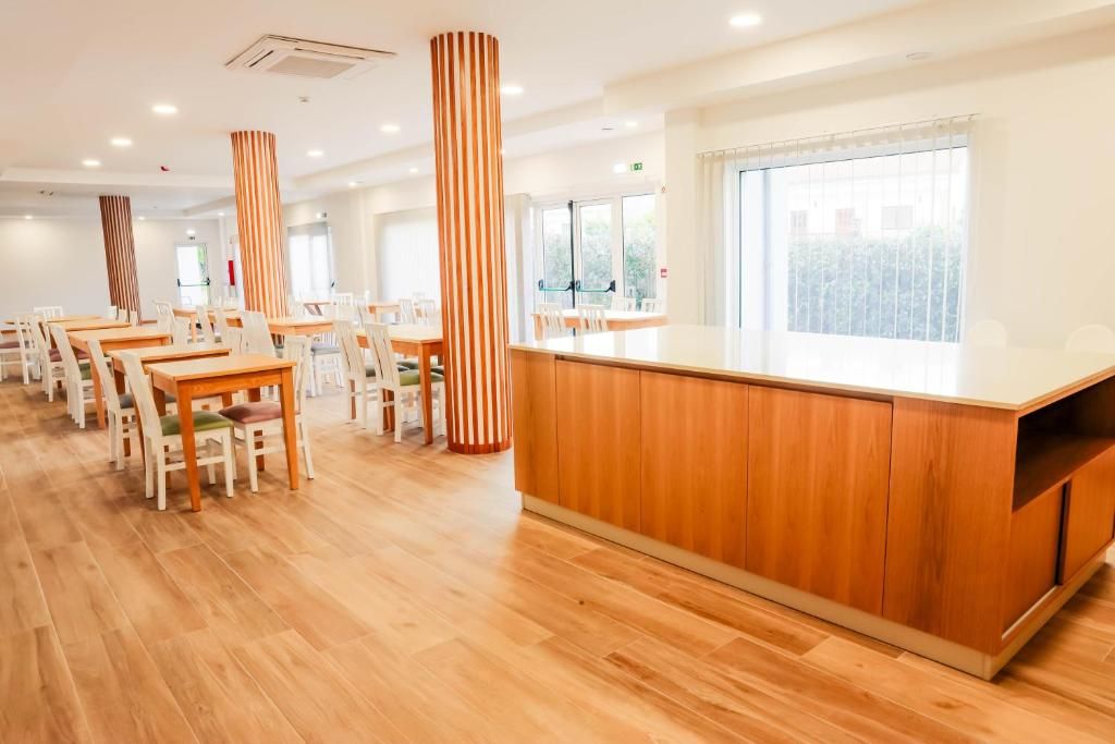 Comedor de hotel con mesas y sillas de madera, una barra central y ventanas amplias.