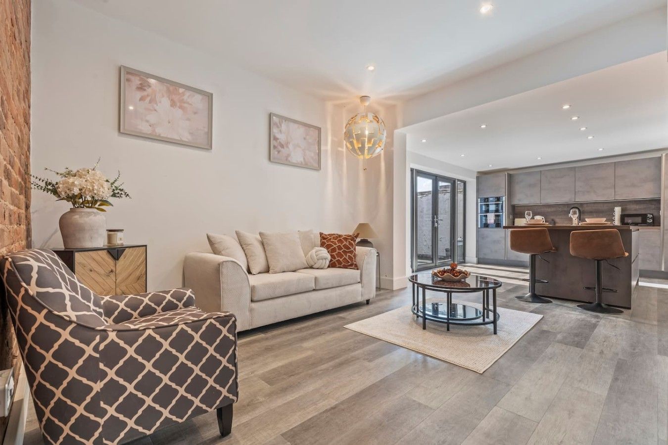 A modern living room with a sofa, a patterned armchair, a coffee table, and a kitchen area with bar stools.