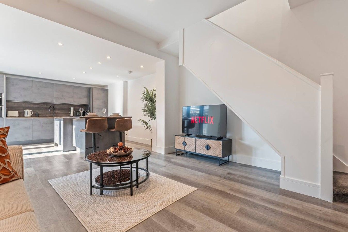 A modern living space with a kitchen, dining area, and a staircase.
