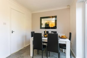 Ein Essbereich mit einem weißen Tisch, schwarzen Stühlen und einem Spiegel an der Wand.