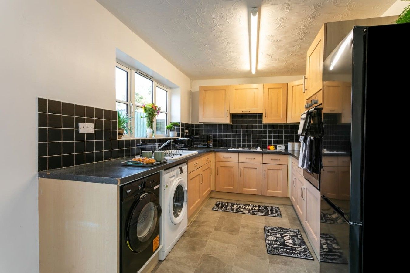 A compact kitchen with a washing machine, a refrigerator, and wooden cabinets.