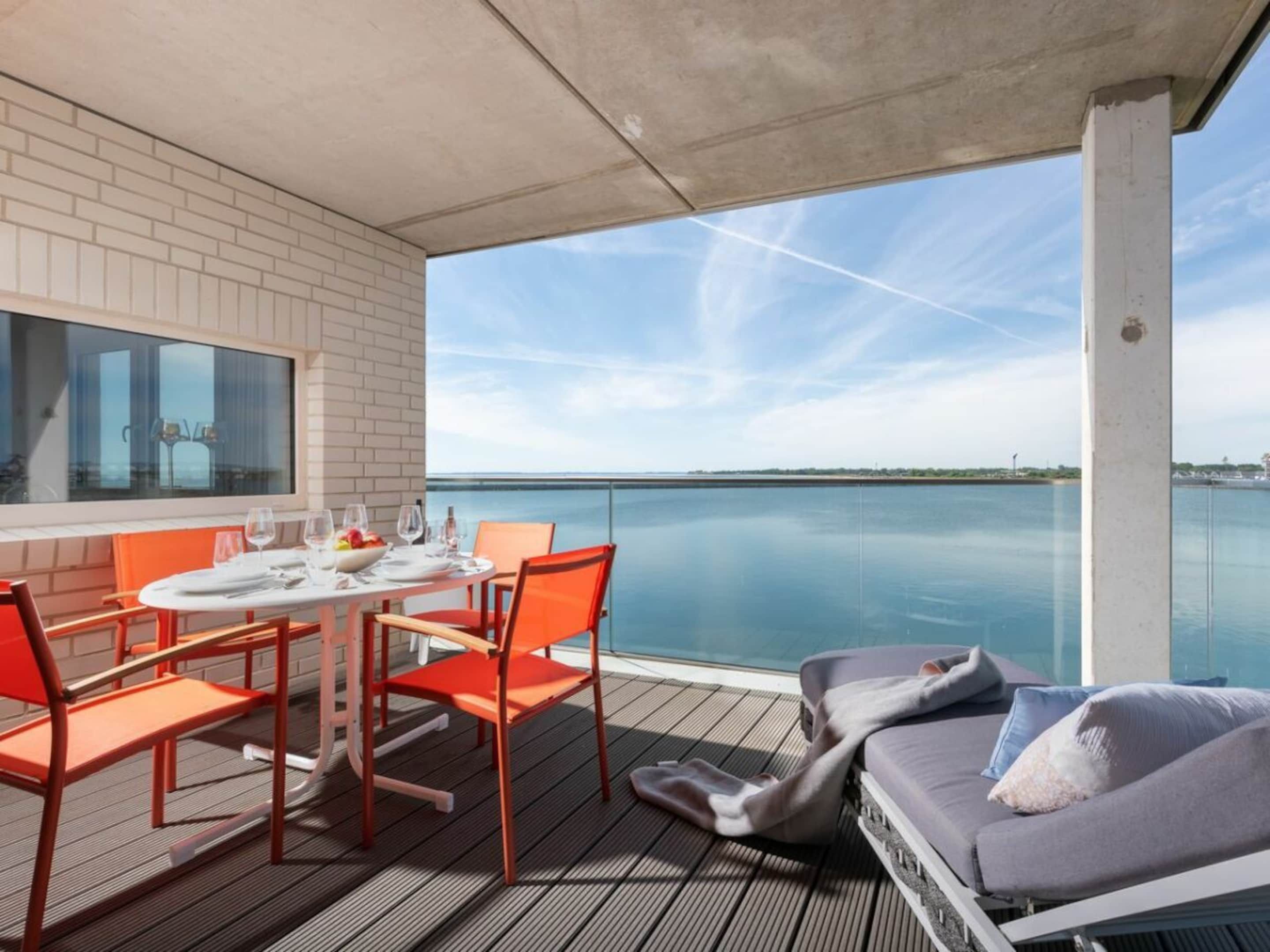A balcony with a table and chairs, a sofa, and a view of the water.