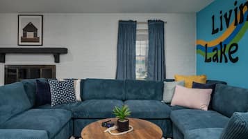 A living room with a sectional sofa, a coffee table with a plant, a fireplace, and a wall with the text 'Living Lake'.