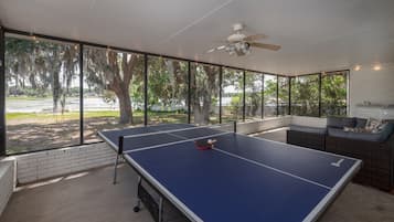 An outdoor ping pong table with a ceiling fan, a brick wall, and a view of trees and water.