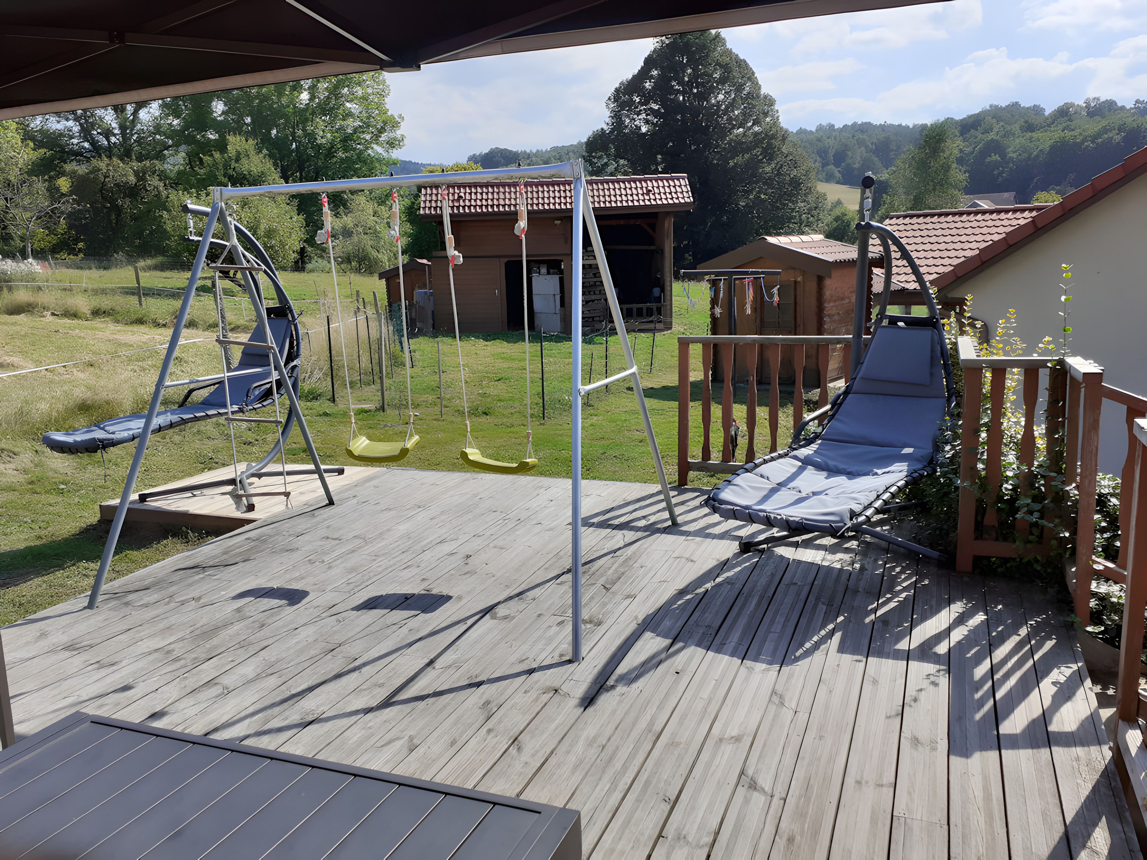 Eine Holzterrasse mit Schaukel, Rutsche und Liegestuhl.