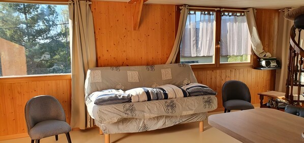 A cozy room with a wooden interior, a bed, two chairs, a table, and a window with curtains.