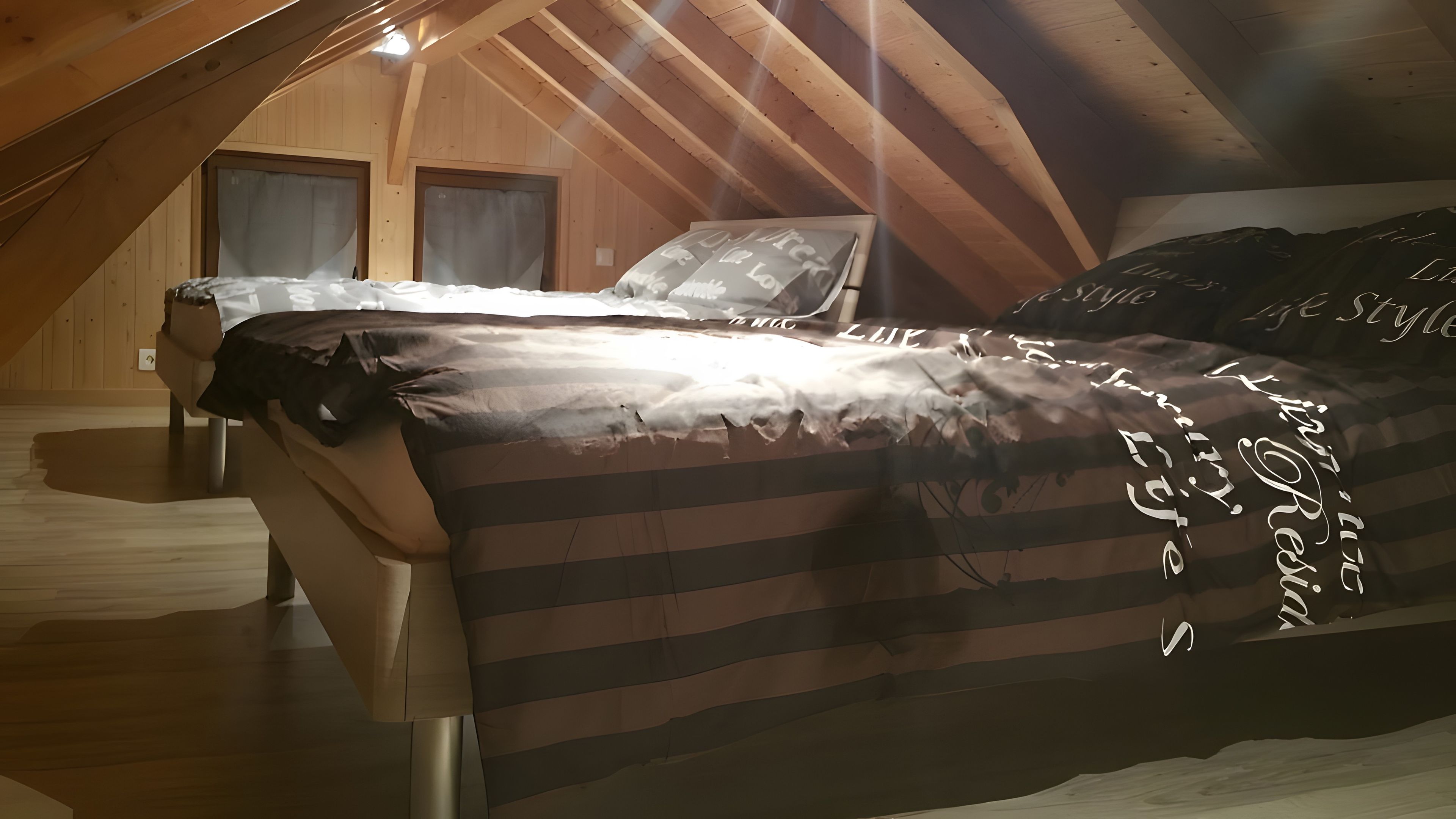 Un dormitorio con techo inclinado, paredes de madera, una cama con colcha a rayas y dos ventanas con cortinas.