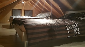 A bedroom with a sloped ceiling, wooden walls, a bed with a striped bedspread, and two windows with curtains. - Cottage 'Gite Aux Zierattes' with Mountain View, Private Terrace and Wi-Fi (Combrimont)