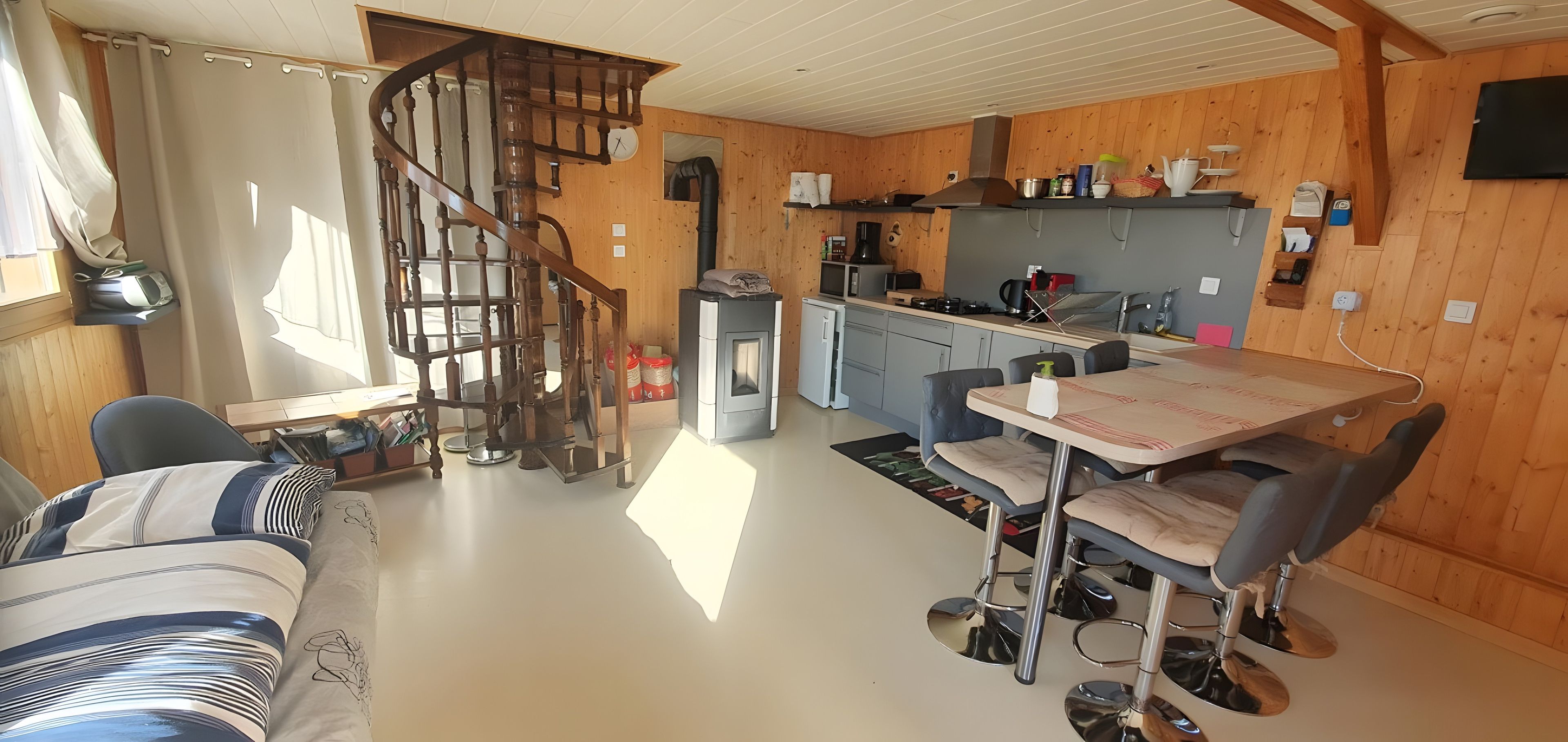 Un interior acogedor con una escalera de caracol, un comedor con mesa y sillas, y un rincón de kitchenette.