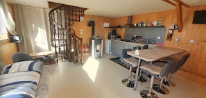 A cozy interior with a spiral staircase, a dining area with a table and chairs, and a kitchenette. - Cottage 'Gite Aux Zierattes' with Mountain View, Private Terrace and Wi-Fi (Combrimont)