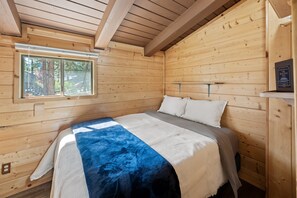 Een houten kamer met een bed, een raam en een plank met een boek.
