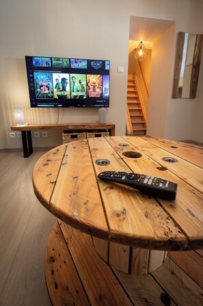 A wooden table with a remote control in front of a flat-screen TV displaying a selection of movies. - New Listing (Remiremont)
