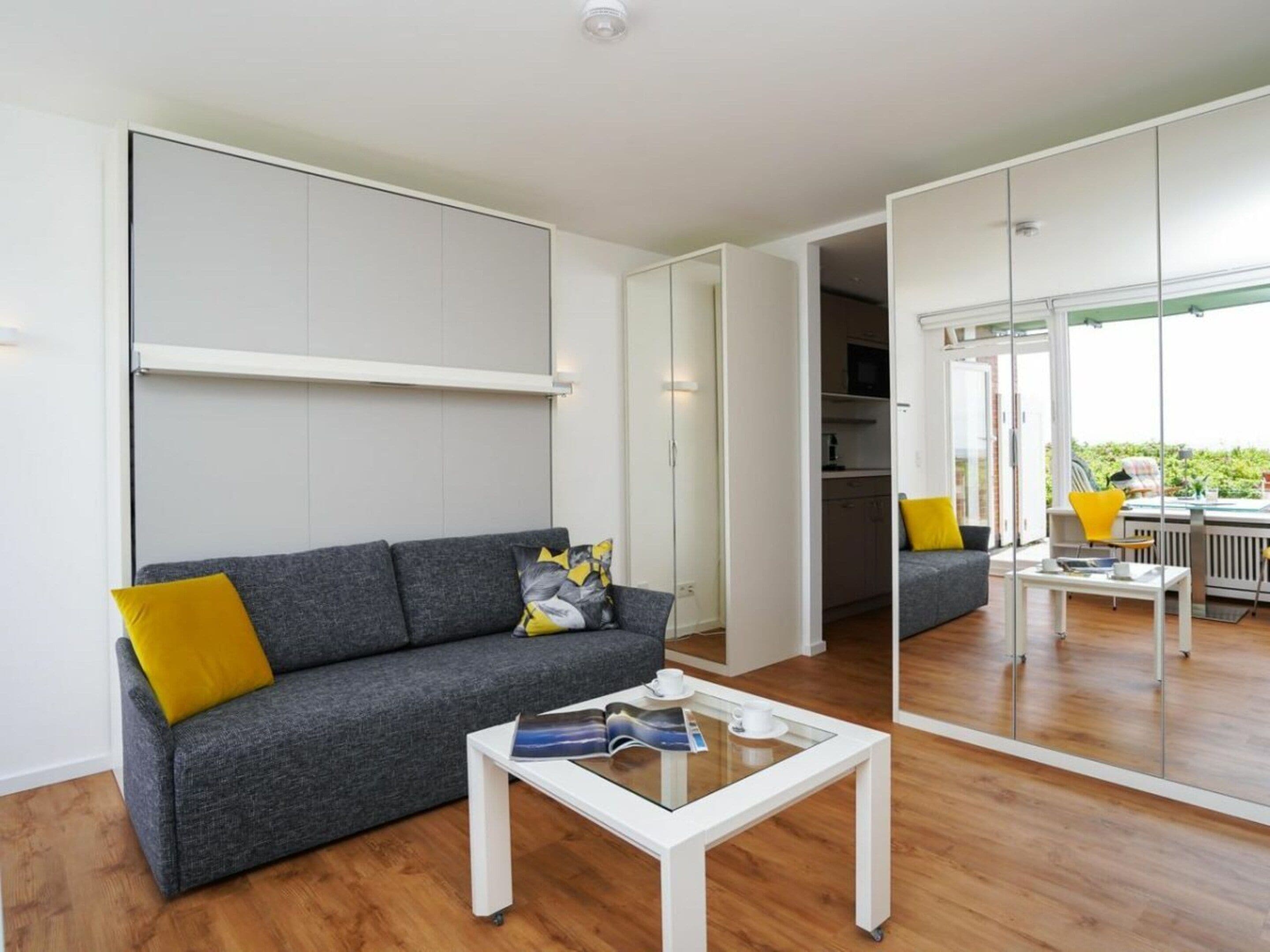 A modern living room with a grey sofa, a coffee table, and a large mirror reflecting the space.