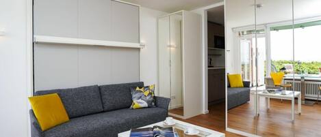 A modern living room with a grey sofa, a coffee table, and a large mirror reflecting the space.