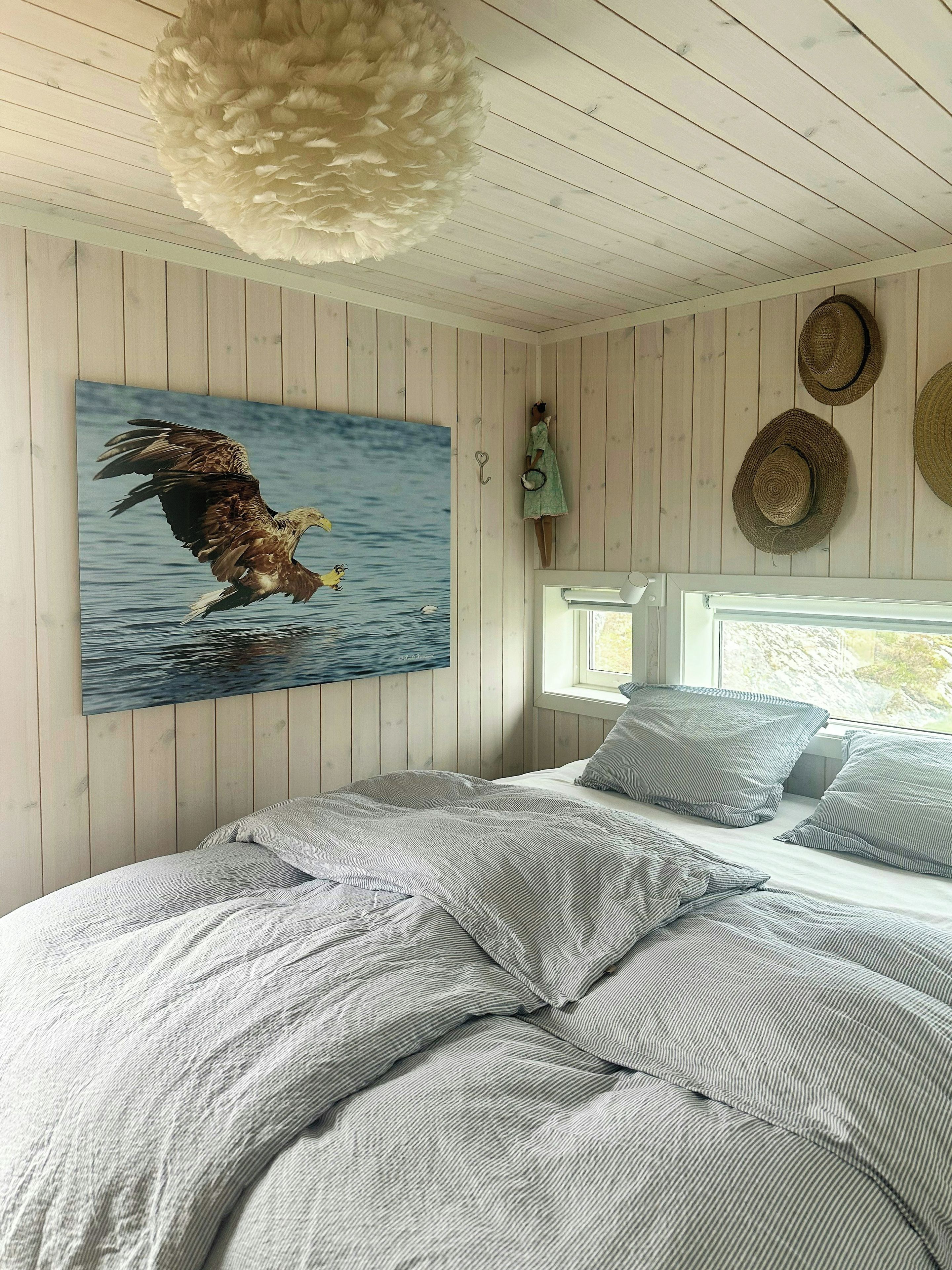 A bedroom with a large bed, a wall-mounted painting of an eagle, and a window with a view.