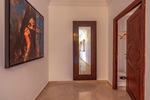 A hallway with a large framed painting on the left, a mirror with a geometric frame, and a wooden door on the right. - Dar Nouraï (marrakech)