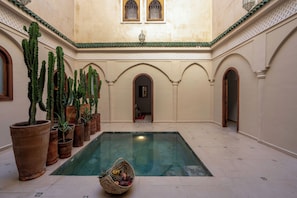 An indoor swimming pool with a tiled floor, surrounded by arched doorways and potted cacti. - Dar Nouraï (marrakech)