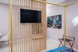 Una habitación con una televisión montada en la pared, una cama con cubrecama azul, una silla y un panel de madera.