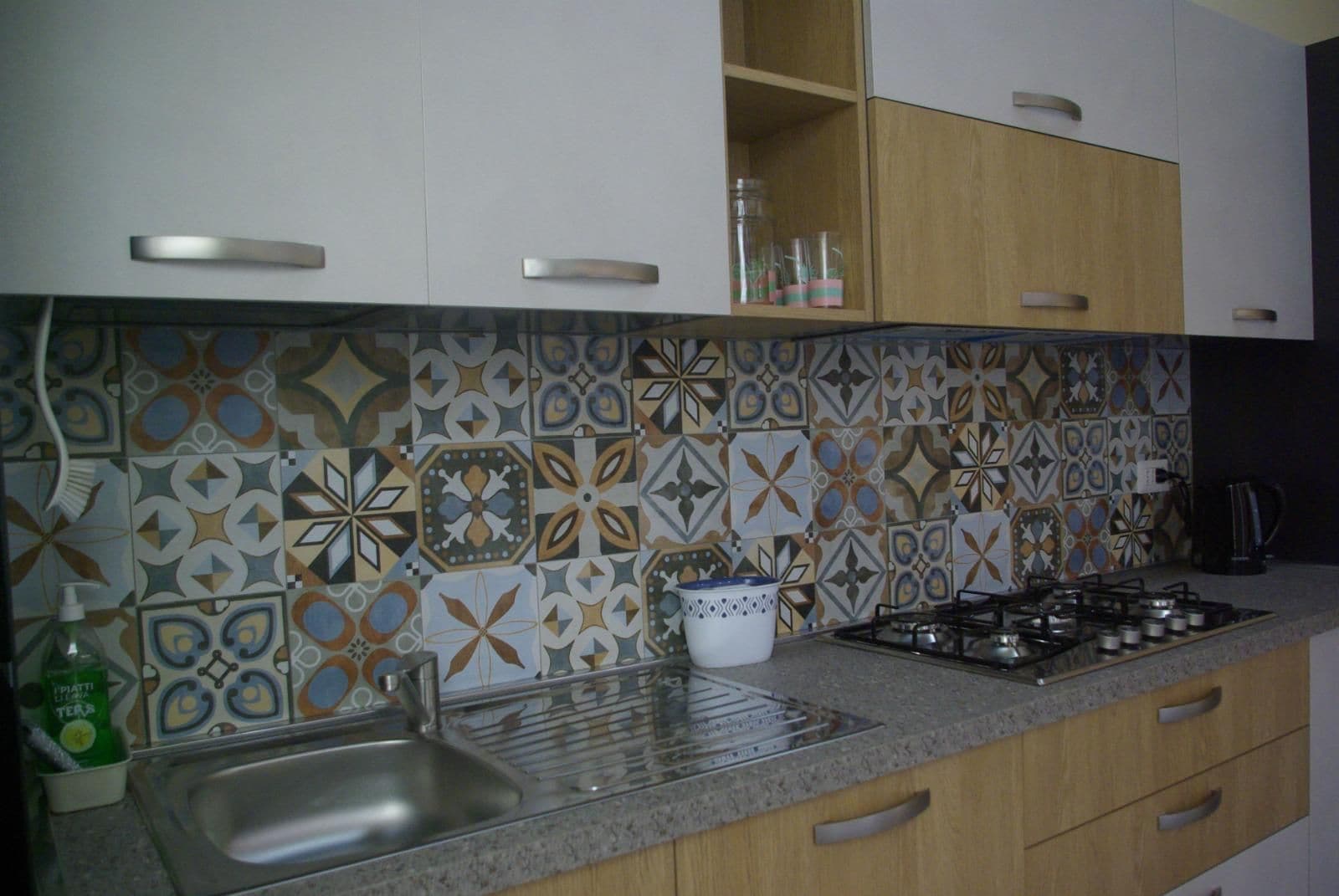 A kitchen with a patterned backsplash, stainless steel sink, and wooden cabinets.