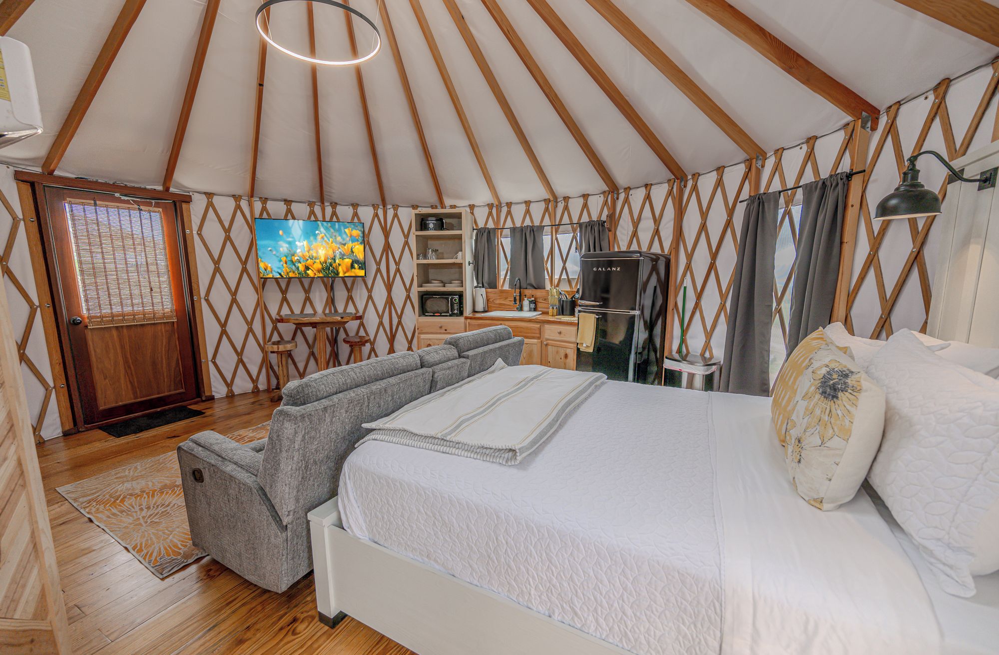Interieur van een joert met een bed, zithoek, kitchenette en een televisie.