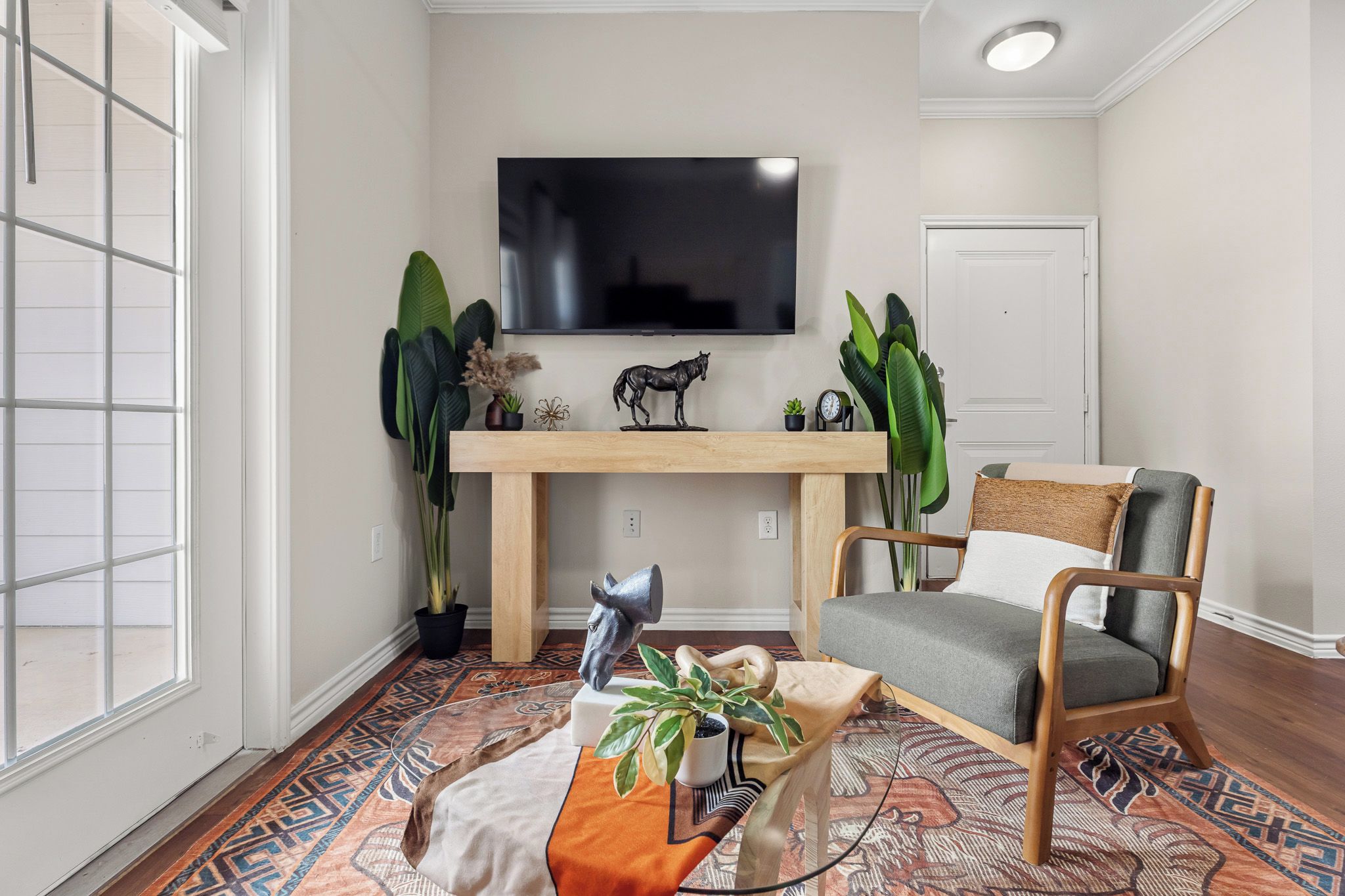 Una sala de estar con un televisor de pantalla plana montado en la pared, una mesa de centro de madera, un sillón y una alfombra estampada.