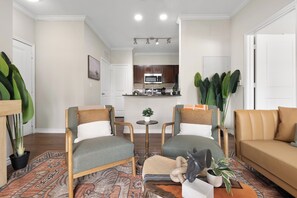 Ein Wohnzimmer mit zwei Sesseln, einem Sofa, einem Couchtisch und einer kleinen Küche im Hintergrund.