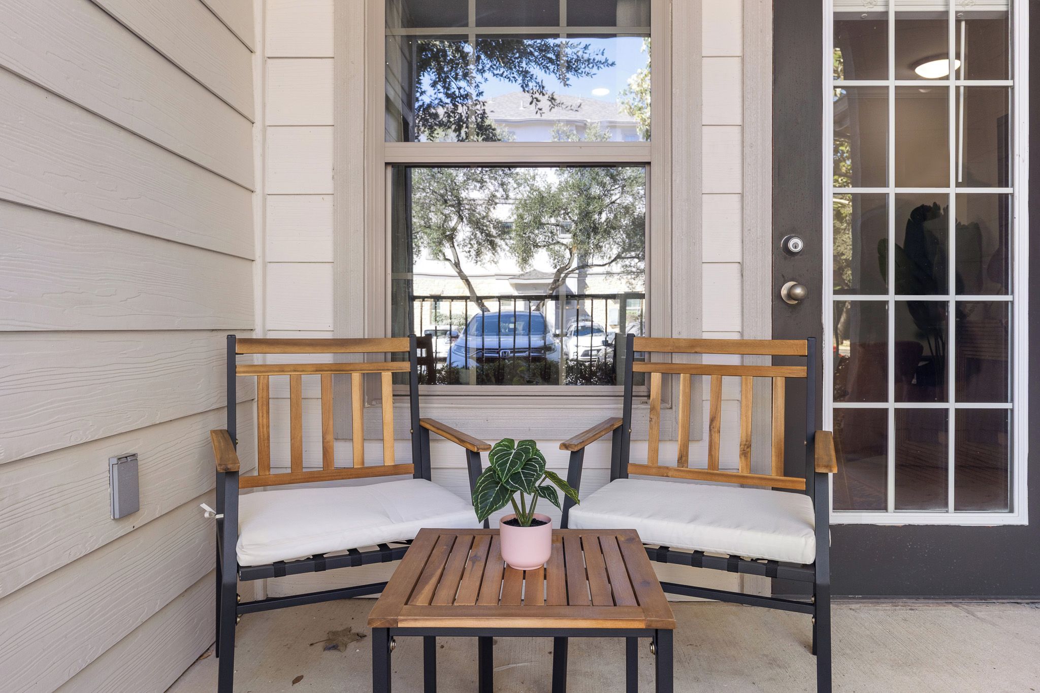 A wooden bench with white cushions and a small table with a potted plant in front of a window.