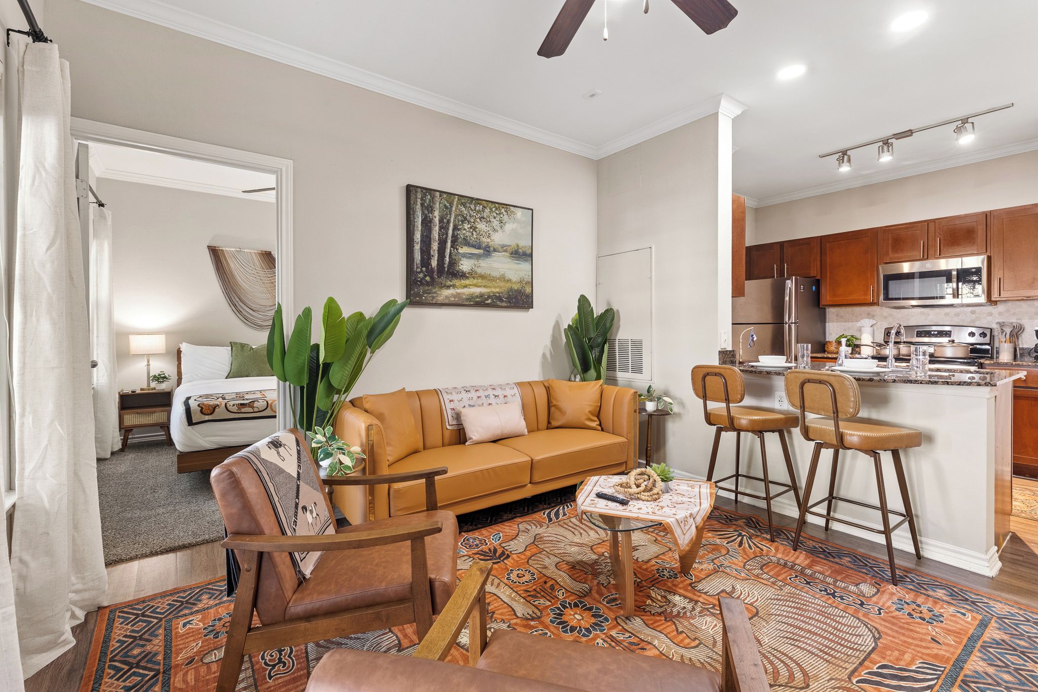 A living room with a sofa, chairs, a coffee table, and a kitchen area with a refrigerator and microwave.