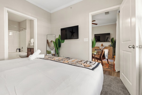 Une chambre d’hôtel avec un grand lit, un téléviseur fixé au mur et une salle de bain visible à travers une porte ouverte.
