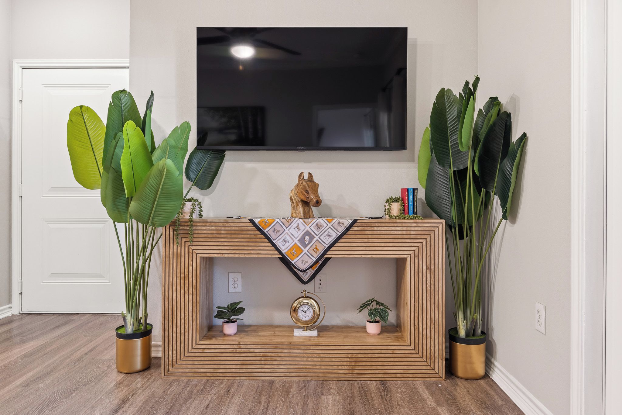 Una sala de estar con una consola de madera, un televisor montado y plantas verdes grandes.