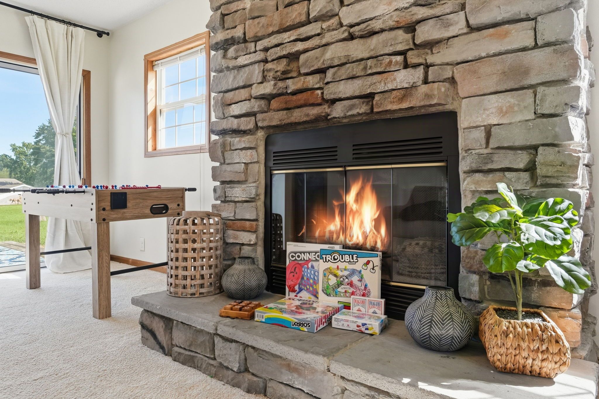 A stone fireplace with a fire, surrounded by various board games and a plant.