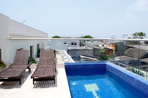 Une piscine sur le toit, dotée de chaises longues et offrant une vue dégagée sur les bâtiments environnants.