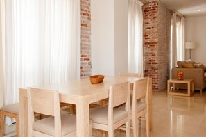 Un coin repas avec une table et des chaises en bois, un mur en briques et un canapé à l’arrière-plan.