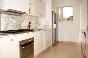 Une cuisine moderne équipée d’une cuisinière à gaz, d’un four, d’un pare-feu en marbre et d’un réfrigérateur en acier inoxydable.