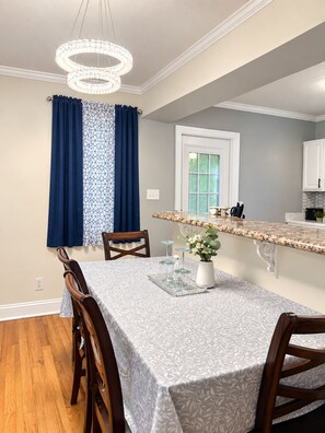 Un coin repas avec une table dressée pour deux personnes, un lustre et une fenêtre avec des rideaux.