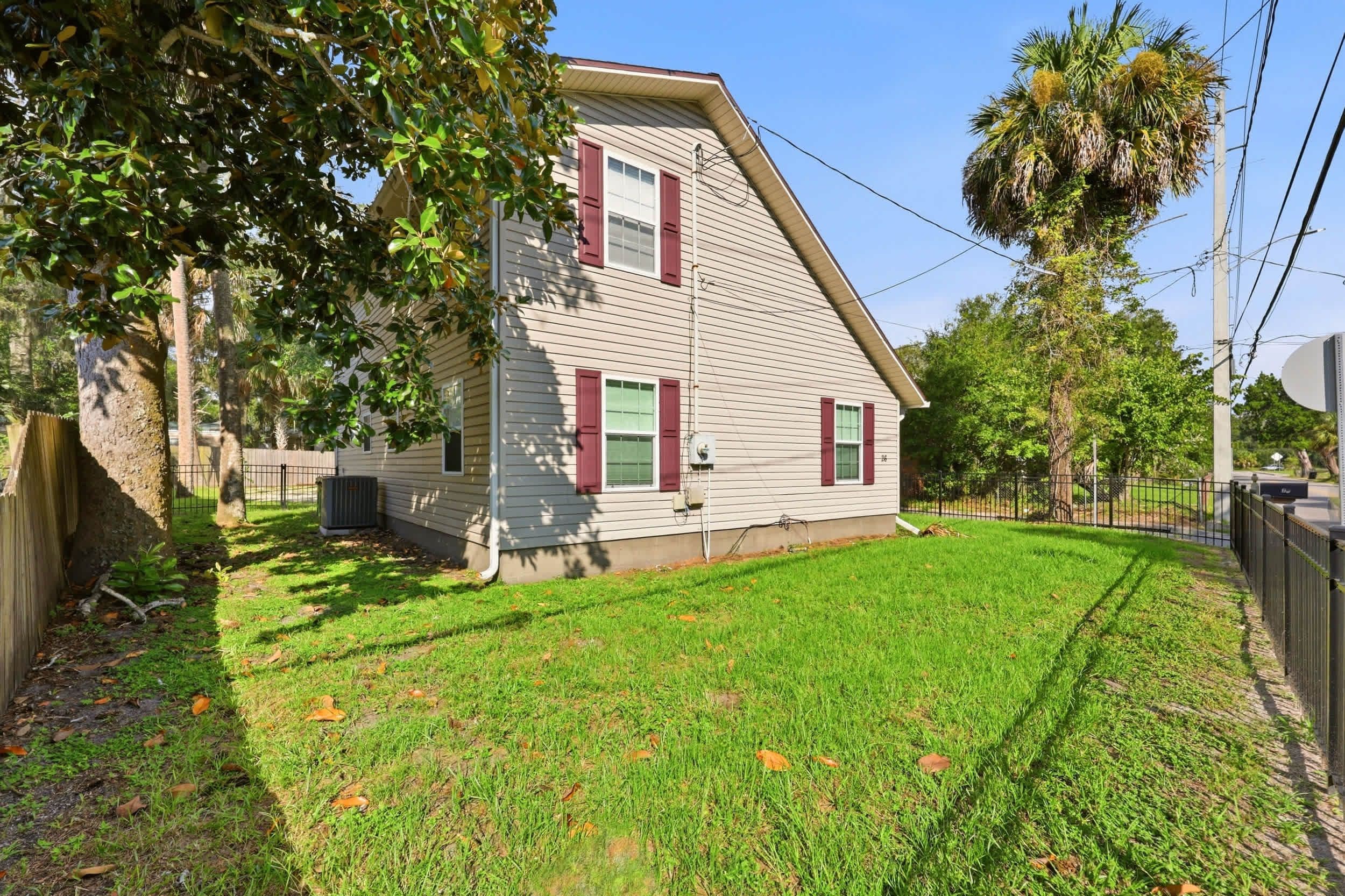 A two-story house with a sloped roof, a fenced yard, and a palm tree.