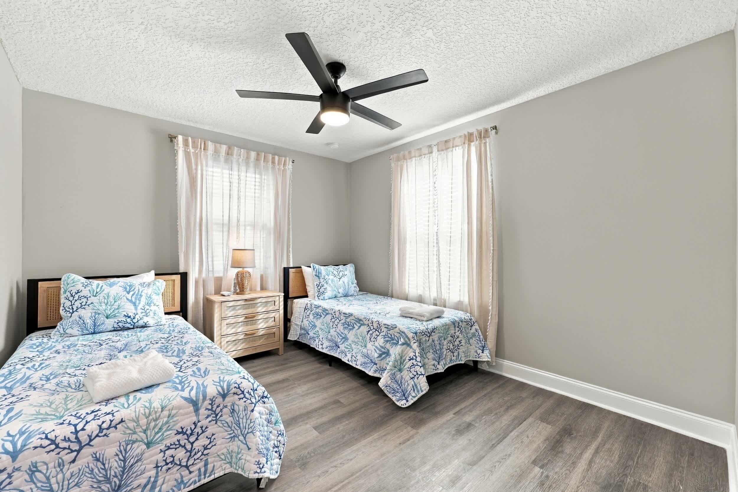 A bedroom with two beds, a ceiling fan, and a nightstand with a lamp.